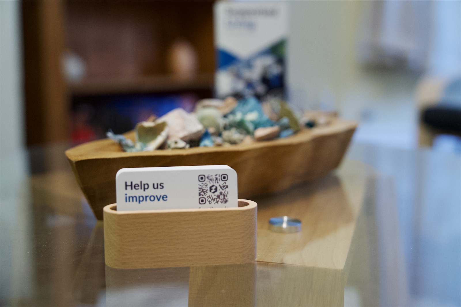 Help us improve feedback card in a wooden holder on a glass table at Eden House.